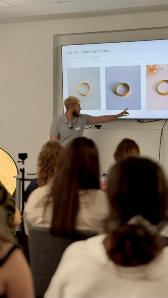 Workshop beim Burger Branchentreff: Ein Referent präsentiert Goldtrauringe auf einer Leinwand vor einem Publikum aus Goldschmieden und Juwelieren. Das Programm umfasst praxisnahe Workshops rund um Edelmetalle und Ringproduktion.