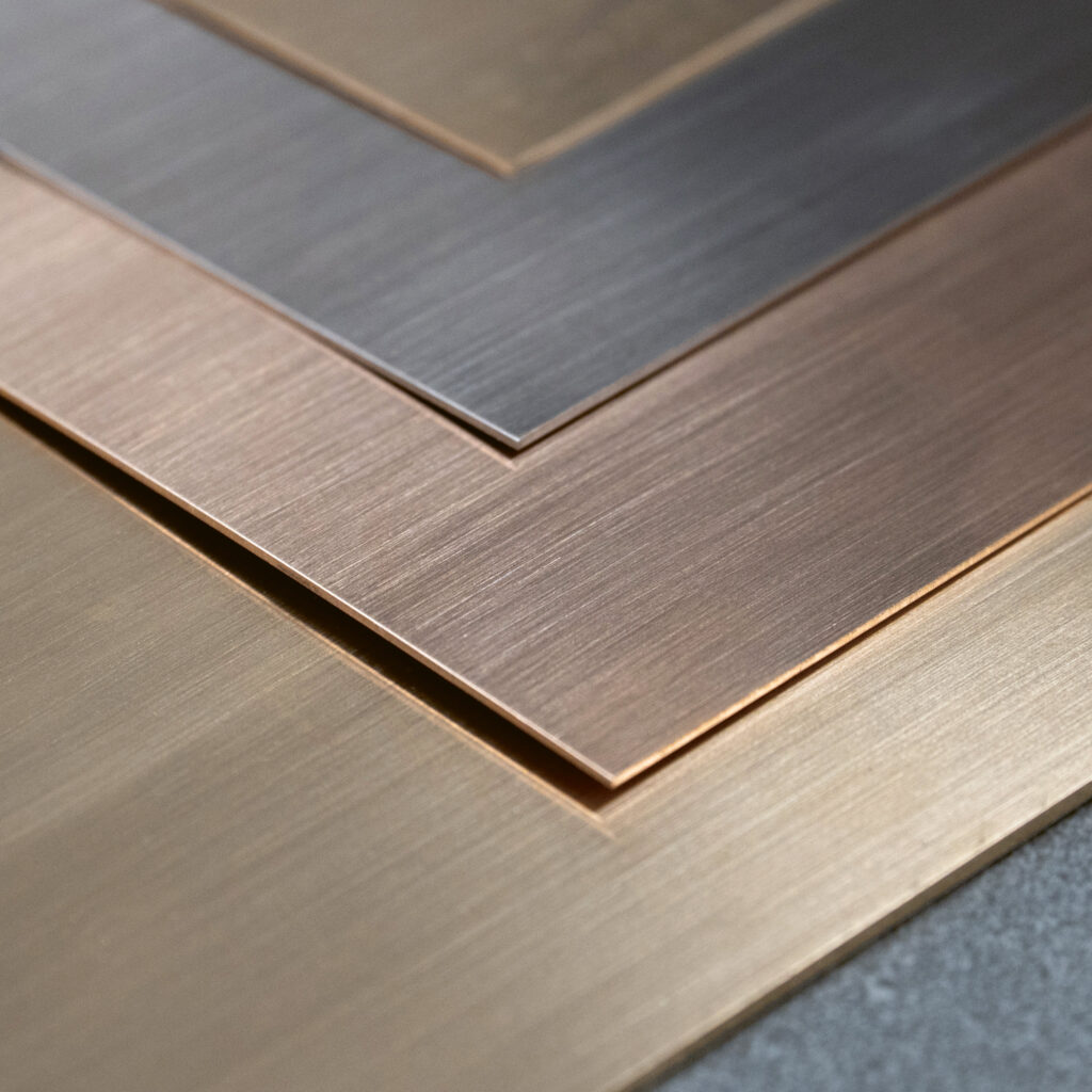 Nahaufnahme von vier sich überlappenden Metallblechen in Gold-, Bronze-, Kupfer- und Silbertönen, jedes mit einer gebürsteten, strukturierten Oberfläche und sauberen, scharfen Kanten.