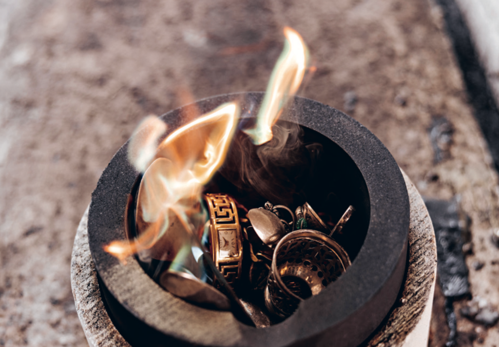 Goldschmuck und Scheidgut werden in einem Tiegel eingeschmolzen, dabei steigen orange Flammen und Rauch auf. Burger Edelmetalle scheidet und verarbeitet Scheidgut jeder Art und rechnet den Edelmetallgehalt zu tagesaktuellen Kursen ab.