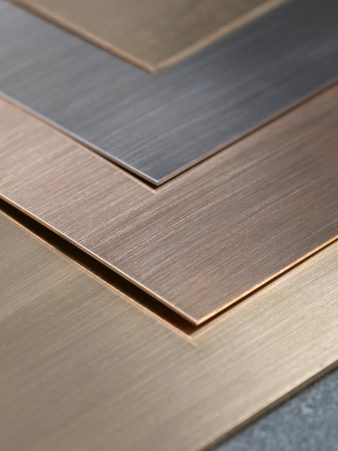 Vier überlappende Edelmetall-Bleche von Burger in Gold-, Silber- und Platintönen mit gebürsteter Oberfläche und scharfen Kanten. Das Blech-Halbzeug wird passgenau zugeschnitten und am nächsten Werktag geliefert.