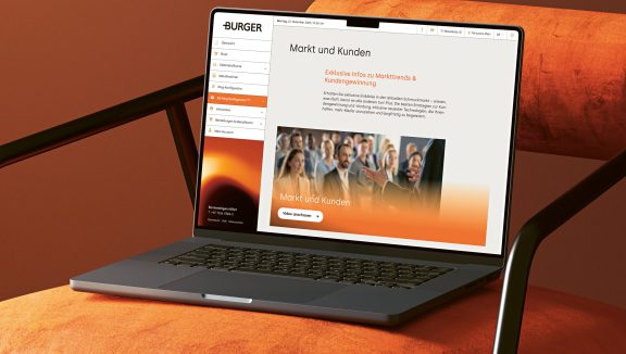 Ein Laptop auf einem orangefarbenen Stuhl zeigt auf der Seite "Markt und Kunden" eine deutsche Website mit Menüpunkten und einem Veranstaltungsfoto, das den Bereich Gekrätz Edelmetall zeigt.