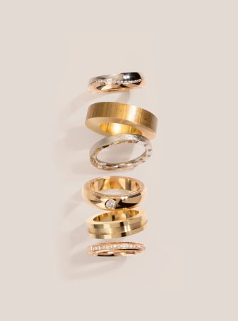 Sechs Trauringe und Ringrohlinge in Gold, Roségold und Silber, teils mit Diamantbesatz, gestapelt auf hellem Hintergrund. Burger Edelmetalle produziert Ringrohlinge und finierte Trauringe in der hauseigenen Ringfertigung.