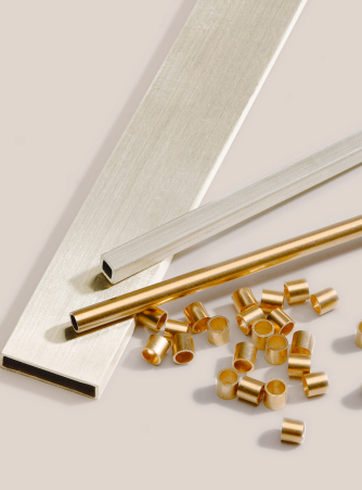 Verschiedene Edelmetall-Rohre in Silber und Gold auf hellem Hintergrund: flache Vierkantprofile, runde Rohre sowie kleine zylindrische Schnittstücke aus Gelbgold. Burger Edelmetalle fertigt Rohre und Profile aus Edelmetall nach Maß in verschiedenen Legierungen und Abmessungen.