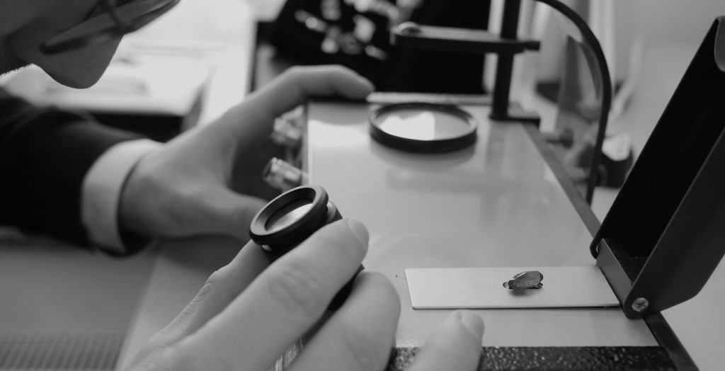 Eine Person untersucht Edelmetalle und Scheidgut mit einem Vergrößerungsglas und Spezialgeräten in einem Labor. Schwarz-Weiß-Foto.