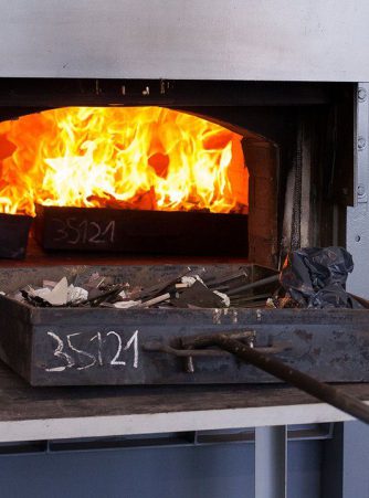 Schublade mit Gekrätz wird in den hauseigenen Veraschungsofen von Burger Edelmetalle eingeführt, im Inneren sind starke Flammen sichtbar. Die Veraschungsanlage wird genutzt, um aus Gekrätz die enthaltenen Edelmetalle zurückzugewinnen.