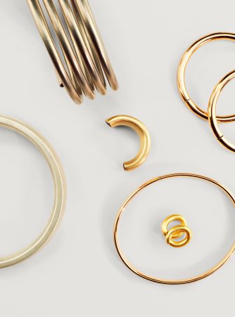 Edelmetall-Wicklungen und Armreifen aus Gold von Burger Edelmetalle, darunter verschiedene Armbänder, Ohrringe und Ringe auf weißem Hintergrund. Das Halbzeug-Sortiment bietet vielfältige Formen für die Schmuckfertigung.