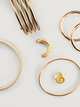 Edelmetall-Wicklungen und Armreifen aus Gold von Burger Edelmetalle, darunter verschiedene Armbänder, Ohrringe und Ringe auf weißem Hintergrund. Das Halbzeug-Sortiment bietet vielfältige Formen für die Schmuckfertigung.